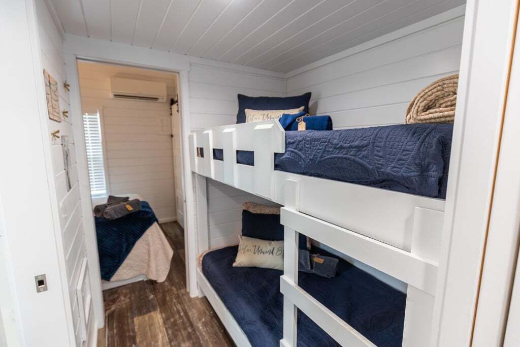 Une chambre avec des lits superposés, aux murs blancs et au plancher en bois.