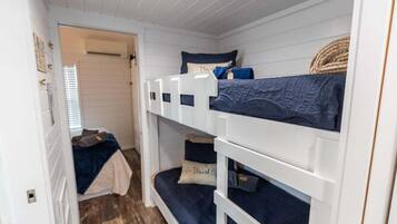 Une chambre avec des lits superposés, aux murs blancs et au plancher en bois.