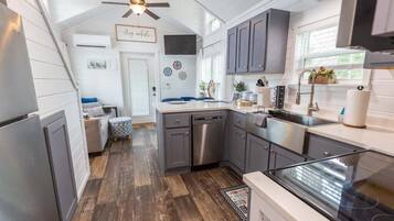 A kitchen with grey cabinets, a dishwasher, and a stove. There is a ceiling fan and a window with plants on the counter.