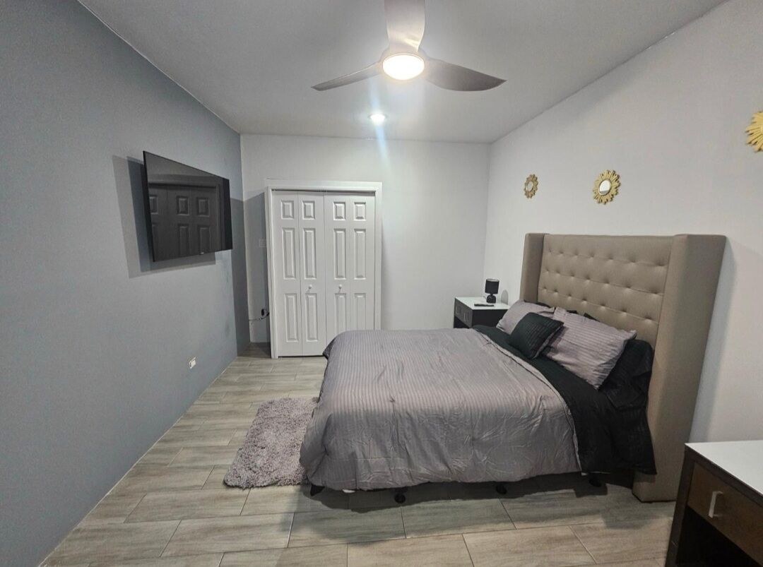 Une chambre à coucher avec un lit, un ventilateur de plafond, une table de chevet et une porte.
