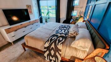 Camera da letto con un letto, una TV, un comodino, una lampada e una finestra con tende.