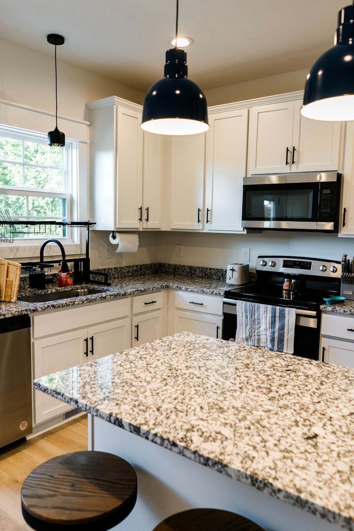 A kitchen with white cabinets, a granite countertop, a stainless steel stove, and a black microwave.