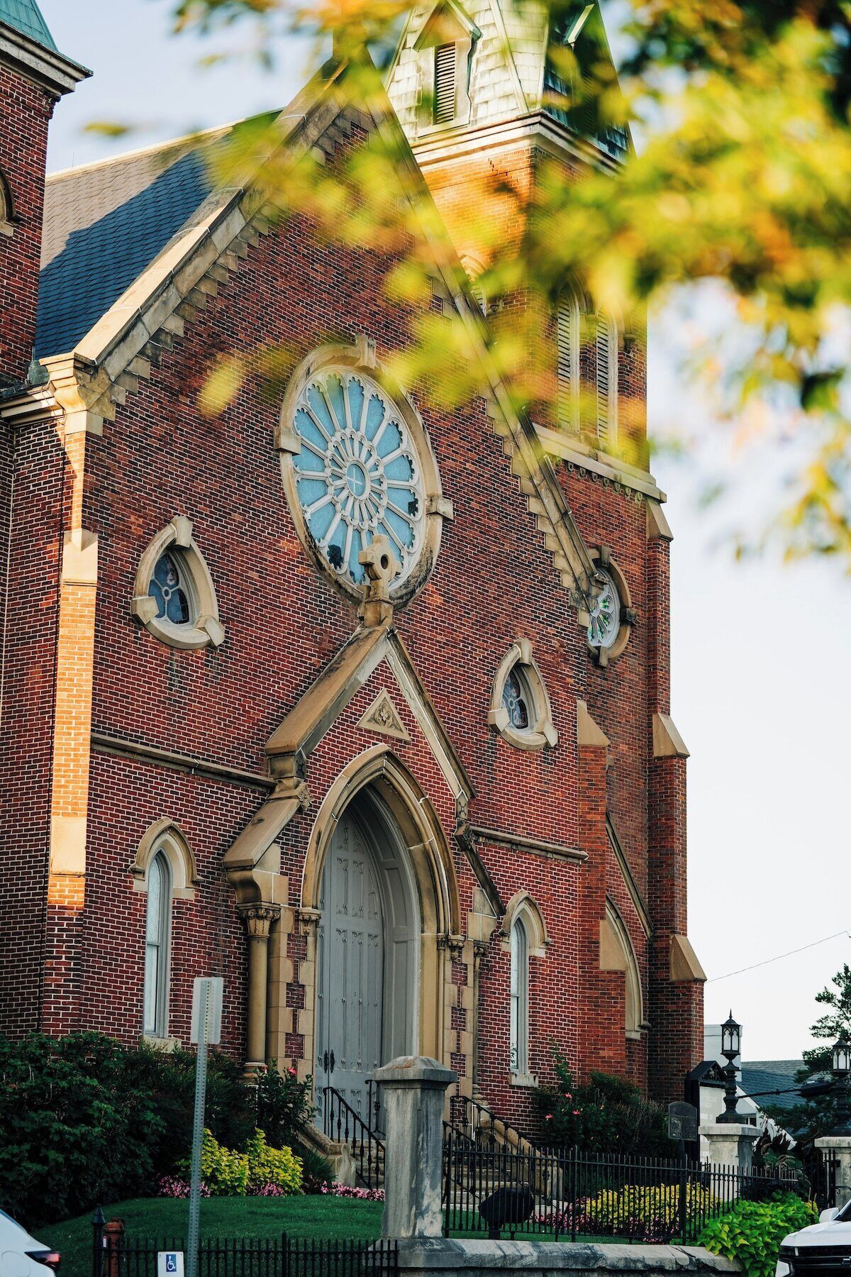 A brick church with a large circular stained glass window, a central entrance with an arched doorway, and a bell tower.