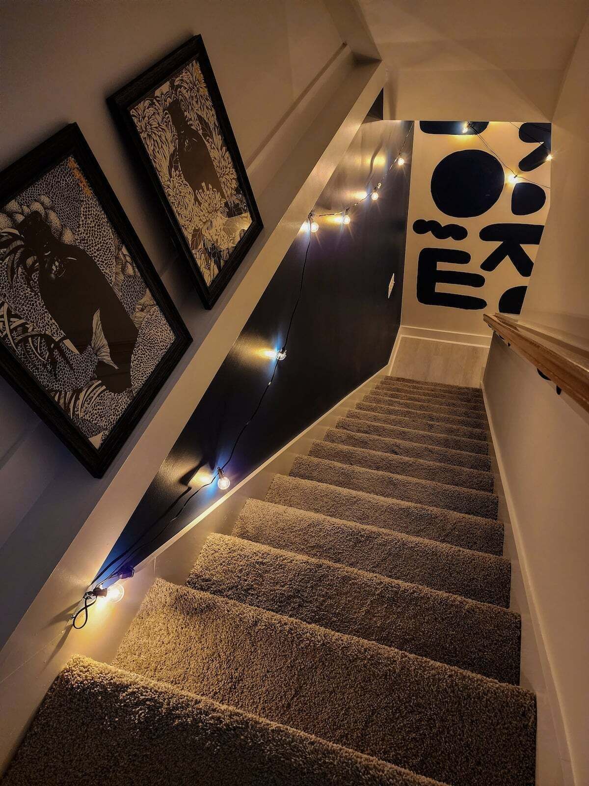 A staircase with carpeted steps, string lights, and framed artwork on the walls.