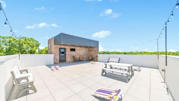 A rooftop patio with a small brick building, outdoor seating, and string lights.