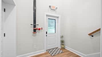A hallway with a white door, a small rug, a potted plant, and an exit sign.
