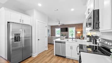 A modern kitchen with stainless steel appliances, white cabinetry, and a wooden floor.