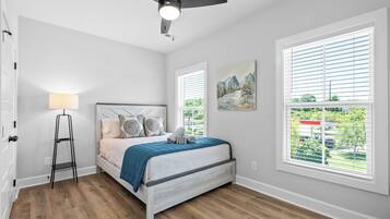 Quarto com cama, abajur, ventoinha no teto e janela com persianas.