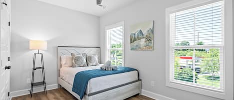 A bedroom with a bed, a standing lamp, a ceiling fan, and a window with blinds.