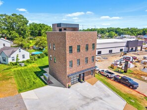 Un immeuble de plusieurs étages, construit en briques, avec un toit plat, un garage et un espace de stationnement où sont garés des véhicules de chantier.
