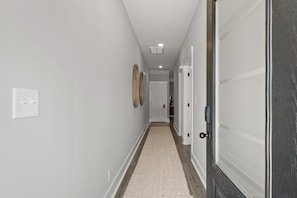 A hallway with a light-colored carpet, white walls, and a wooden floor. There are two doors on the right, one of which is open. - River's Edge (111 Hickory Grove BLVD) (Clarksville)