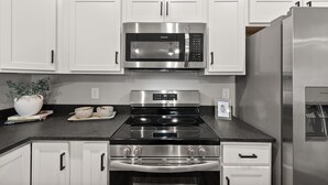 A kitchen with white cabinets, a stainless steel microwave, a stove, and a refrigerator. - River's Edge (111 Hickory Grove BLVD) (Clarksville)