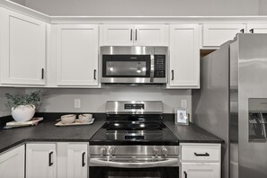 A kitchen with white cabinets, a stainless steel microwave, a stove, and a refrigerator. - River's Edge (111 Hickory Grove BLVD) (Clarksville)