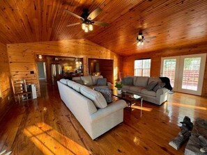A spacious living room with wooden walls and floors, a large sofa, a smaller sofa, and a coffee table. - Cottage on Cypress Bay near Paris Landing State Park (Buchanan)