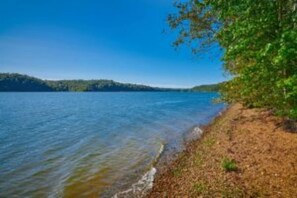 A lakeside view with a clear sky, calm water, and a dirt path along the shore. - Cottage on Cypress Bay near Paris Landing State Park (Buchanan)