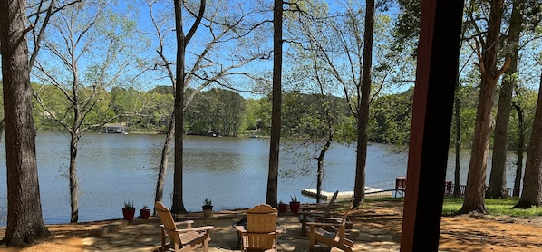 Un espace extérieur aménagé avec des chaises et des tables en bois, offrant une vue sur un lac paisible bordé d’arbres.