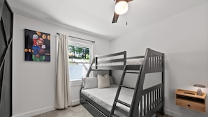 Un dormitorio con literas, una ventana con cortinas, un ventilador de techo y un estante en la pared con una lámpara.