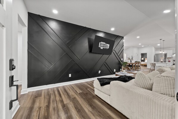 A modern living room with a black accent wall, a mounted TV, a white sofa, and a wooden floor.