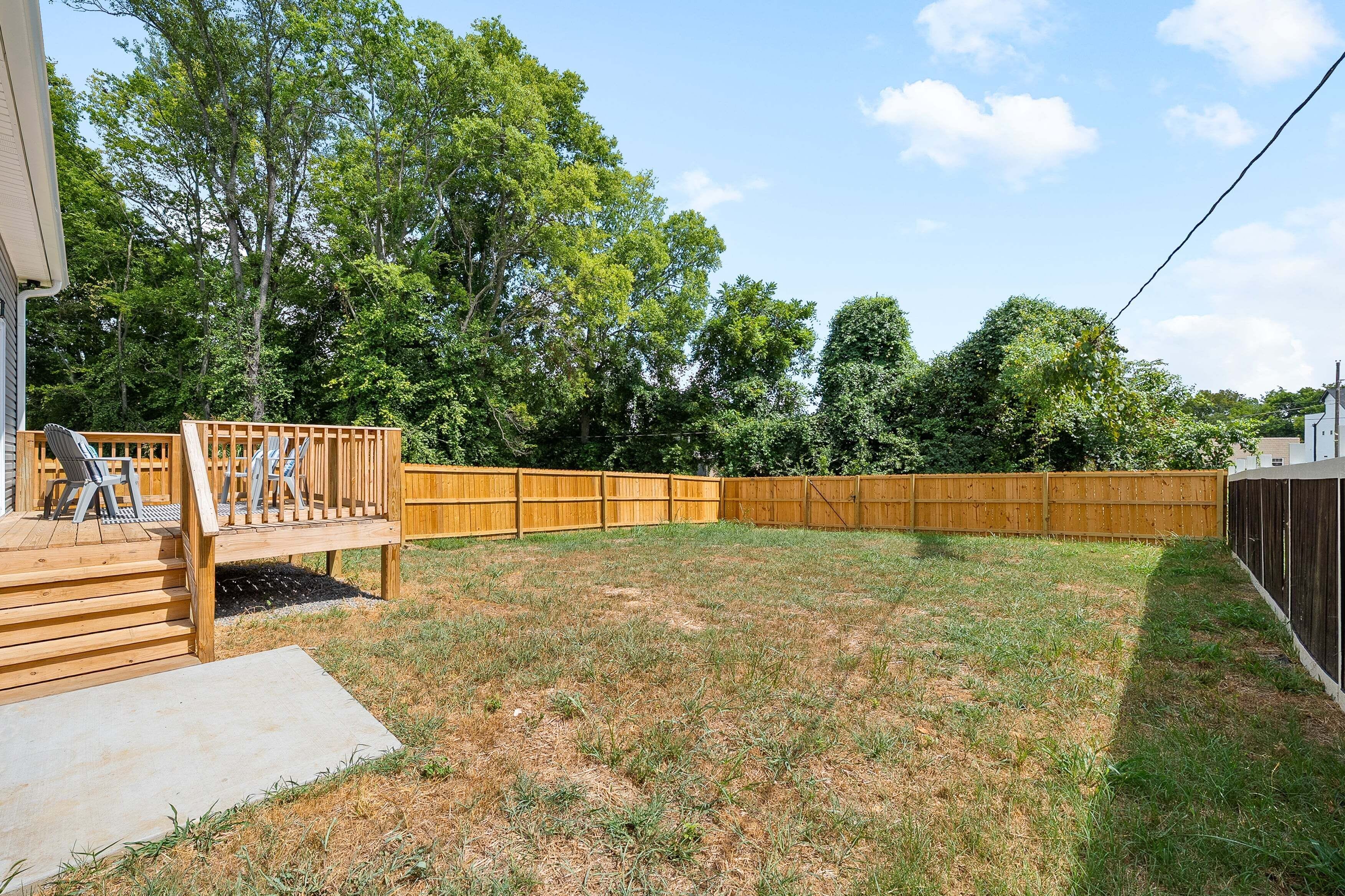 A backyard with a wooden deck, a fenced area, and a grassy lawn.