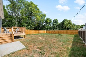 A backyard with a wooden deck, a fenced area, and a grassy lawn.