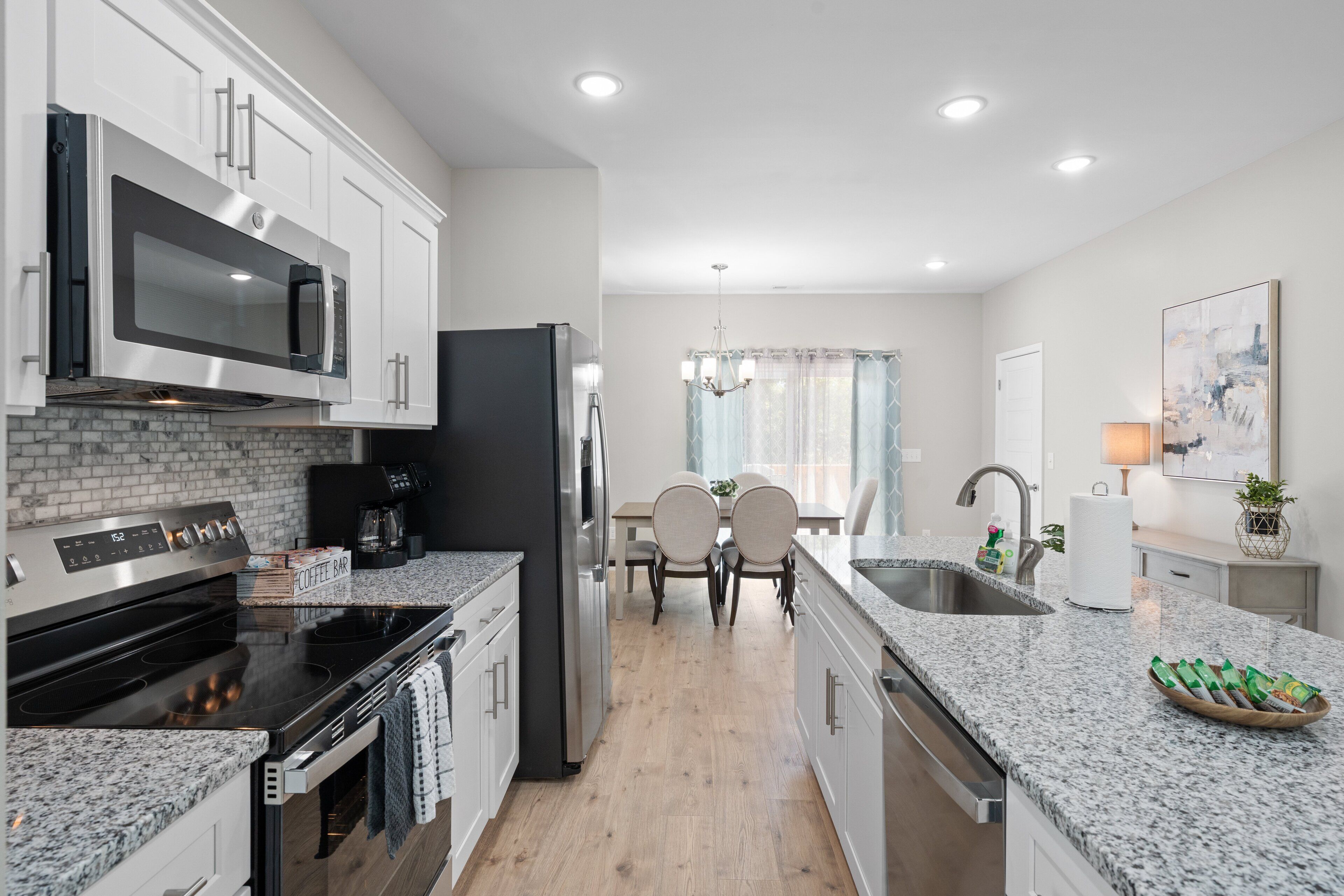 A modern kitchen with white cabinets, a stainless steel microwave, a black refrigerator, a built-in oven, and a granite countertop.