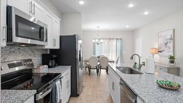 A modern kitchen with white cabinets, a stainless steel microwave, a black refrigerator, a built-in oven, and a granite countertop.