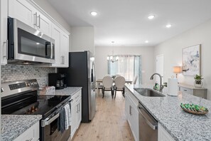 A modern kitchen with white cabinets, a stainless steel microwave, a black refrigerator, a built-in oven, and a granite countertop.