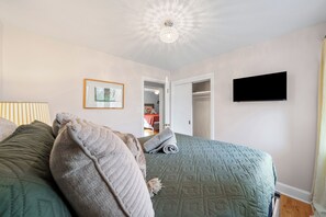 Ein Schlafzimmer mit einem Bett, Kissen, einem Flachbildfernseher, einem gerahmten Bild und einer Deckenleuchte.