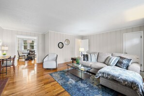 A living room with a sofa, armchair, coffee table, and a dining area with chairs and a table.