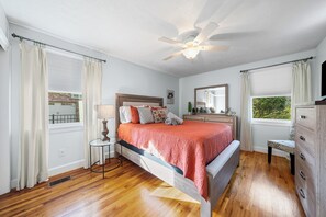 A bedroom with a bed, a nightstand, a dresser, a ceiling fan, and a window with curtains.