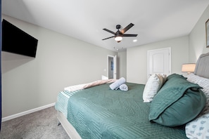 A bedroom with a bed, a ceiling fan, a wall-mounted TV, and a door. - Main Street Manor | Spacious Home Near Dining (1022 Main Street) (Clarksville)