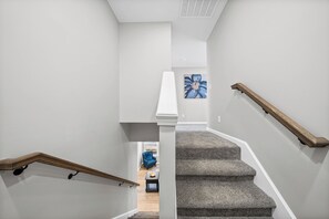 Un escalier avec une rampe en bois, des marches recouvertes de moquette et une chaise bleue en arrière-plan.