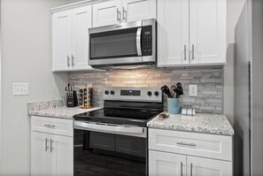 A kitchen with white cabinets, a stainless steel microwave, a stove, and a tiled backsplash.