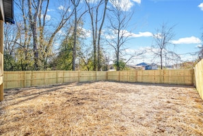 A fenced outdoor area with a dry straw-covered ground, surrounded by trees and a wooden fence. - Main Street Manor | Spacious Home Near Dining (1022 Main Street) (Clarksville)