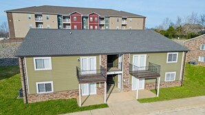 A two-story apartment building with a flat roof, multiple balconies, and a brick foundation.