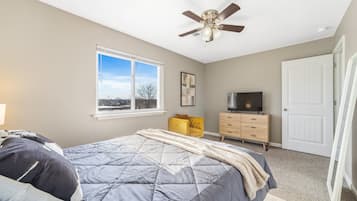 A bedroom with a bed, a ceiling fan, a dresser, a television, and a window with a view.