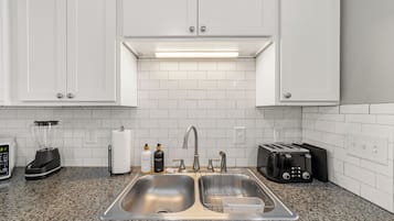 A kitchen with white cabinets, a double sink, a toaster, and a blender.