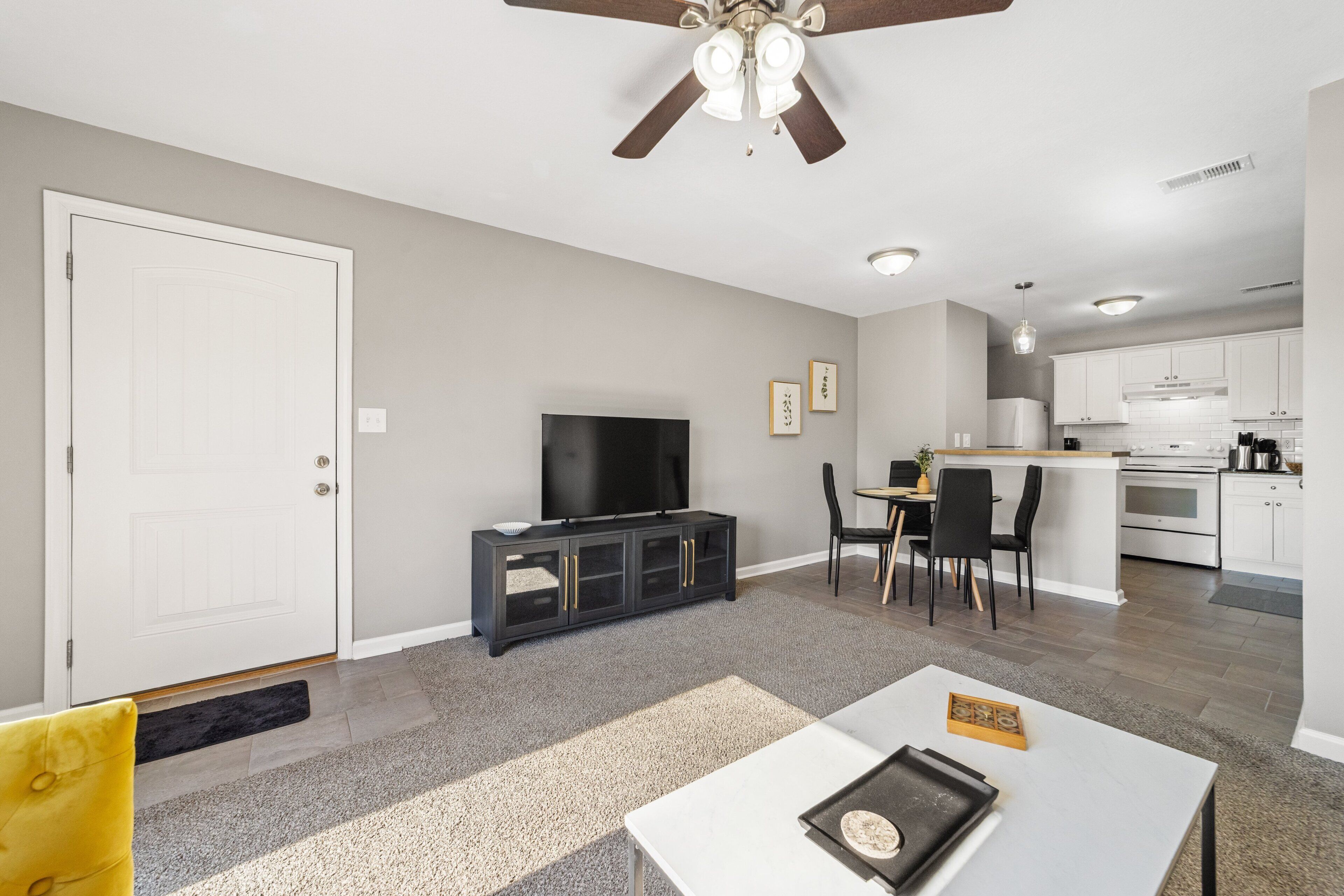 Una sala de estar moderna con un televisor de pantalla plana, un mueble de madera oscura y un comedor con una pequeña mesa y sillas.
