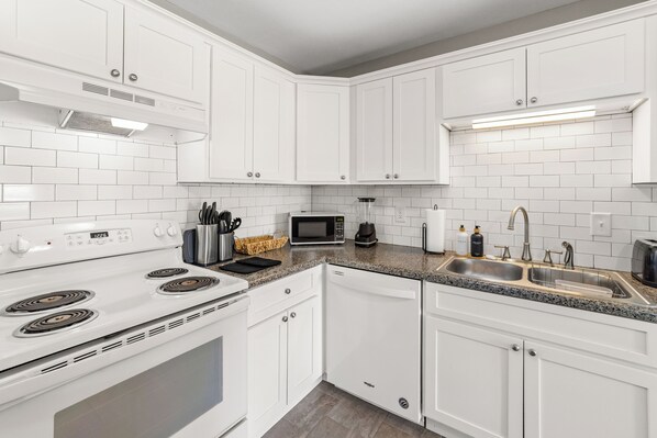 A modern kitchen with white cabinets, a stainless steel sink, a microwave, and a stove.