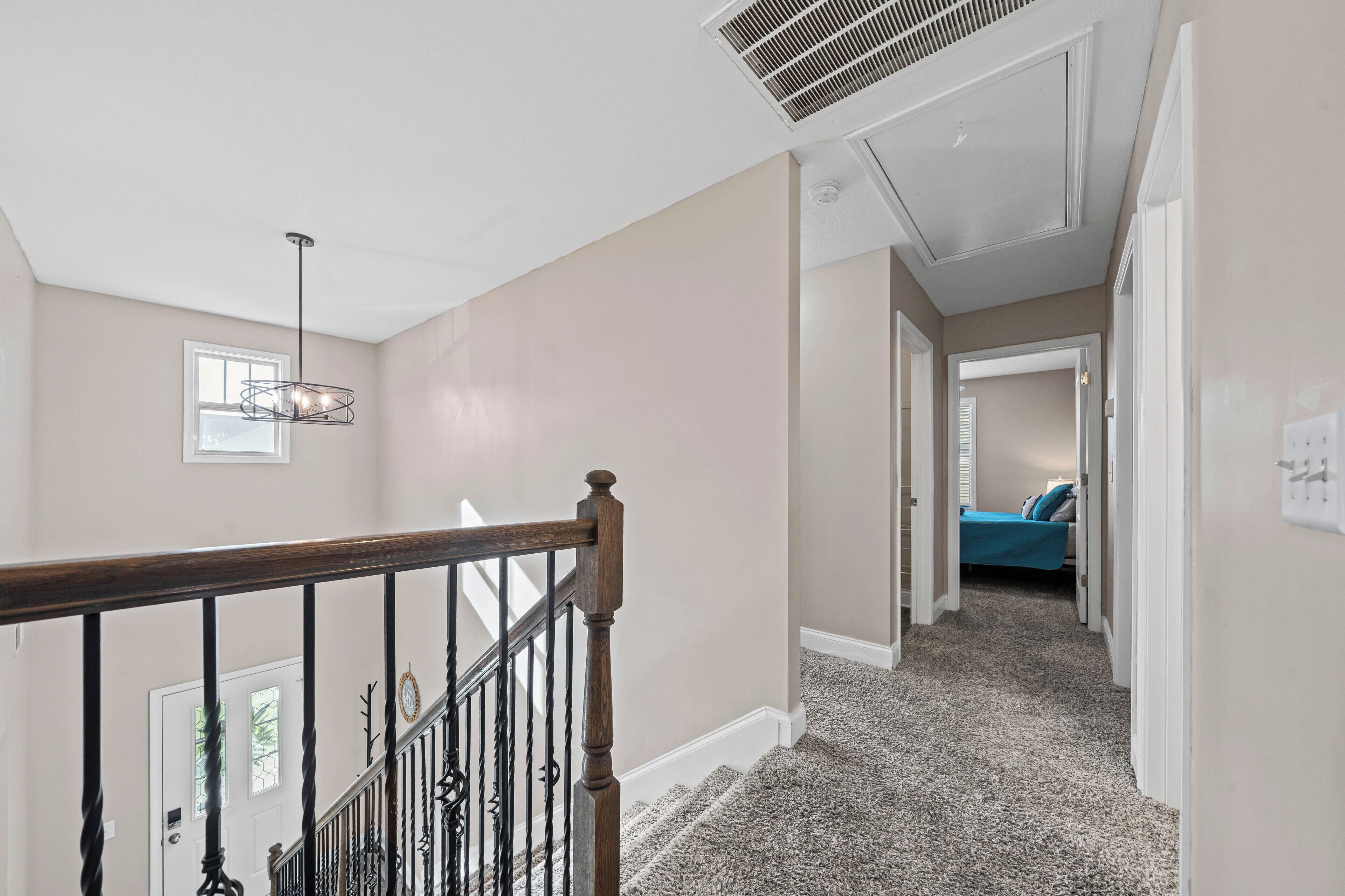 A hallway with a carpeted floor, a wooden railing, and a ceiling vent.