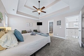 Une chambre à coucher comprenant un lit, un ventilateur de plafond, une télévision et une porte donnant sur un balcon.