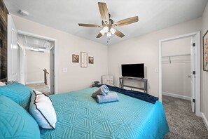 Une chambre à coucher avec un lit, un ventilateur de plafond, une télévision et une porte.