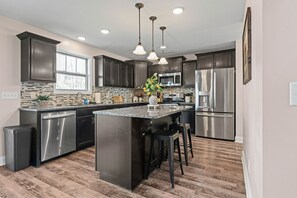A modern kitchen with dark cabinets, stainless steel appliances, and a central island with bar stools. - Month-to-Month Rental (Corporate Stays) (Clarksville)