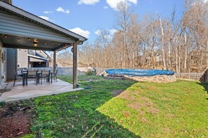 A covered patio area with outdoor furniture, a stone wall, and a grassy yard with trees in the background. - Month-to-Month Rental (Corporate Stays) (Clarksville)