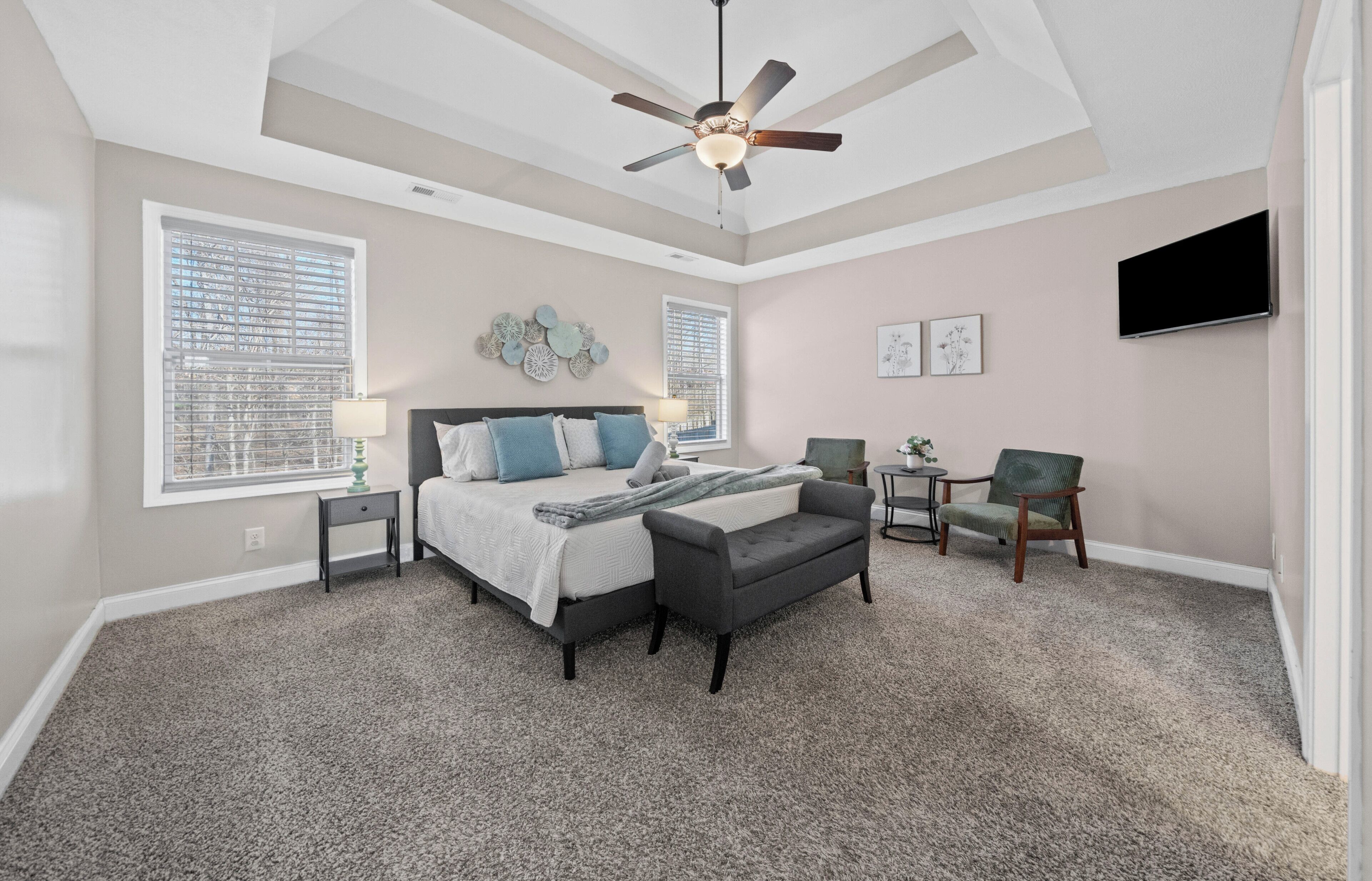 A bedroom with a bed, a desk, a chair, a ceiling fan, and a TV.