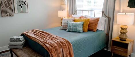 A neatly arranged bedroom with a bed, bedside tables, a bench, and artwork on the walls.