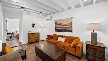 A living room with a sofa, a coffee table, a lamp, a wall-mounted deer head, and a window with curtains.