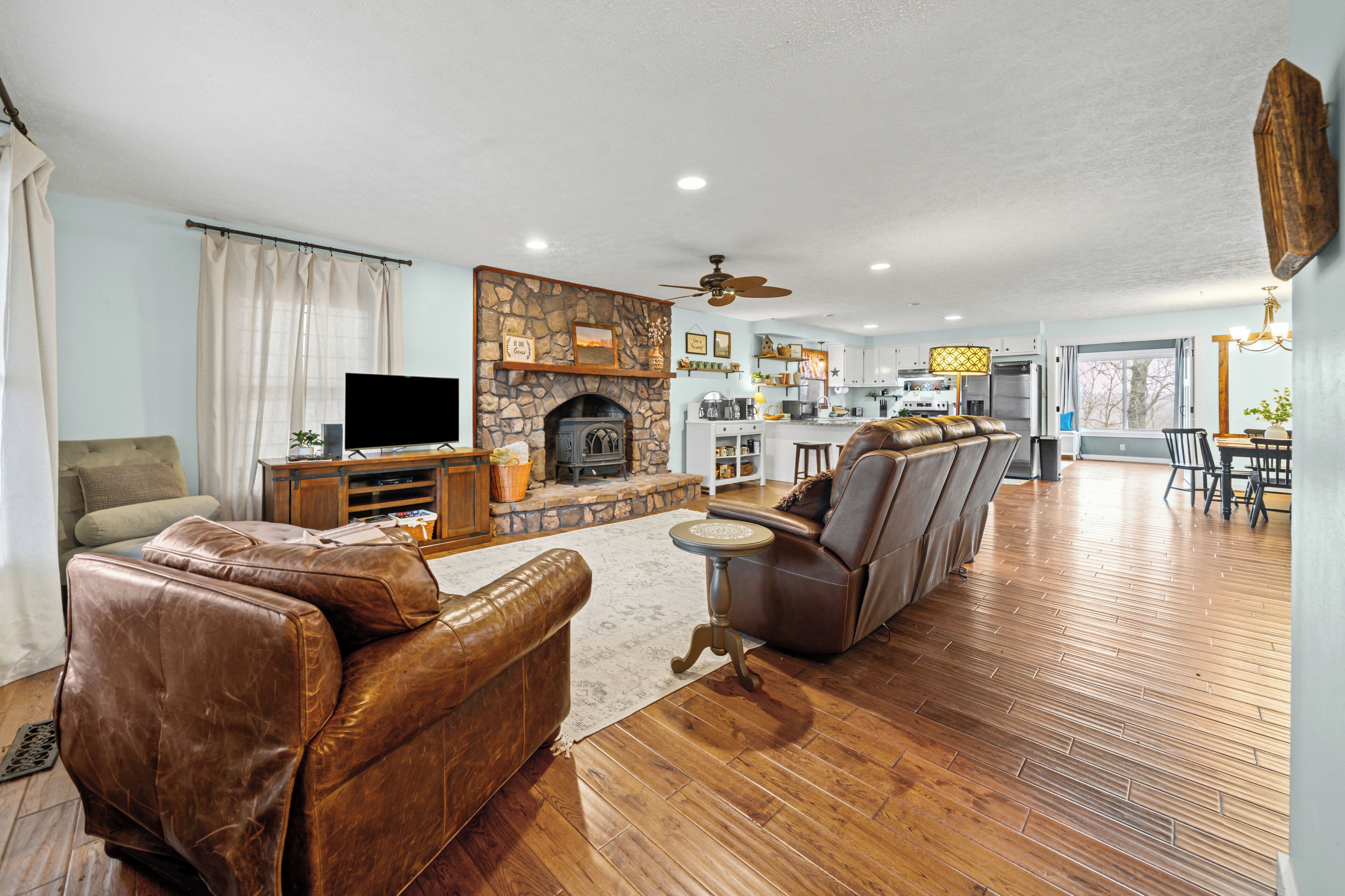 Una amplia sala de estar con chimenea, sofás de cuero, televisor y un comedor con candelabro.