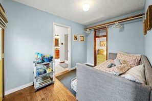 A bedroom with a grey sofa, a wooden dresser, and a small hallway leading to a bathroom.