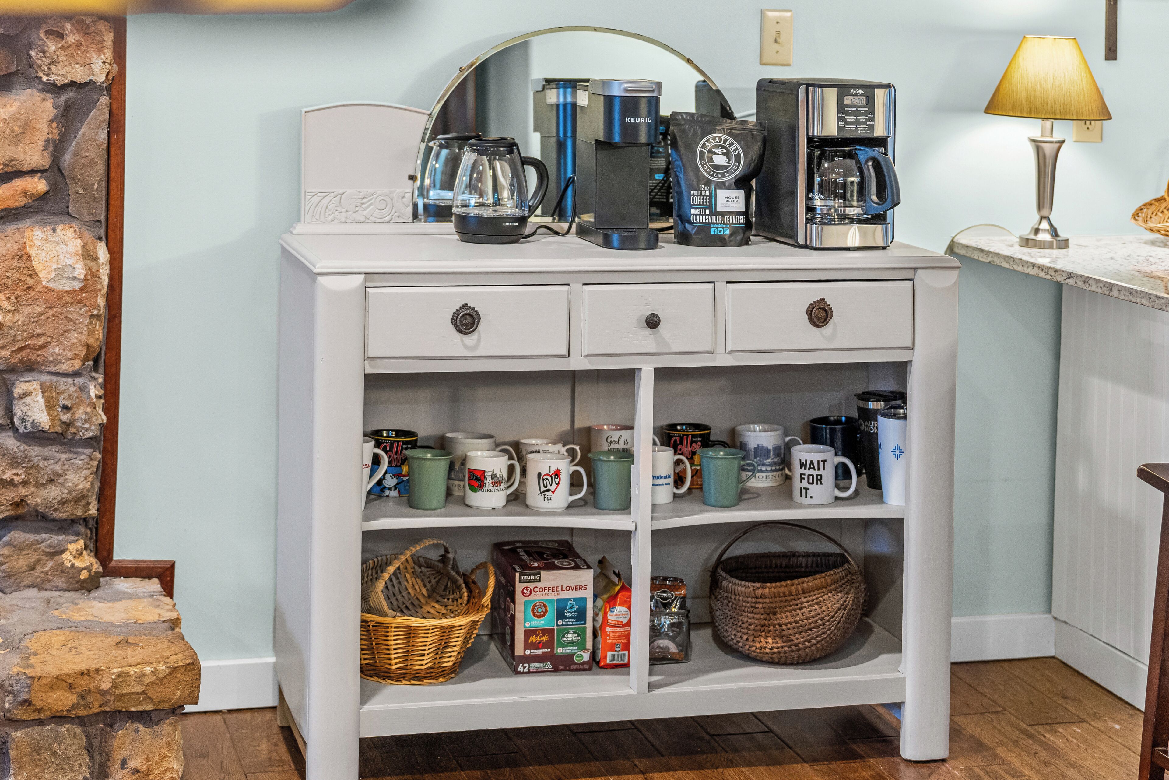 A white wooden cabinet with multiple shelves, containing various coffee makers, mugs, and coffee-related items.